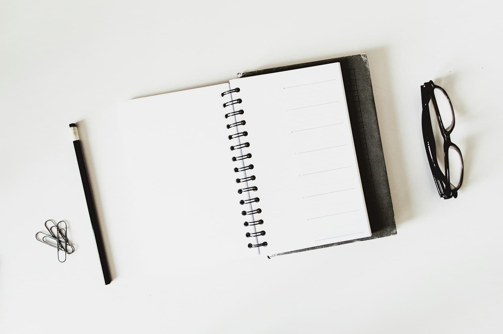 Open notebook, pen and glasses on a white desk